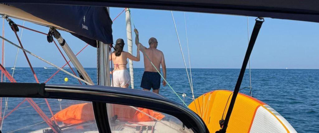 Momento tranquilo en la proa Pareja de espaldas en la proa de un velero disfrutando del mar en un día tranquilo, con tabla de paddle surf en cubierta.